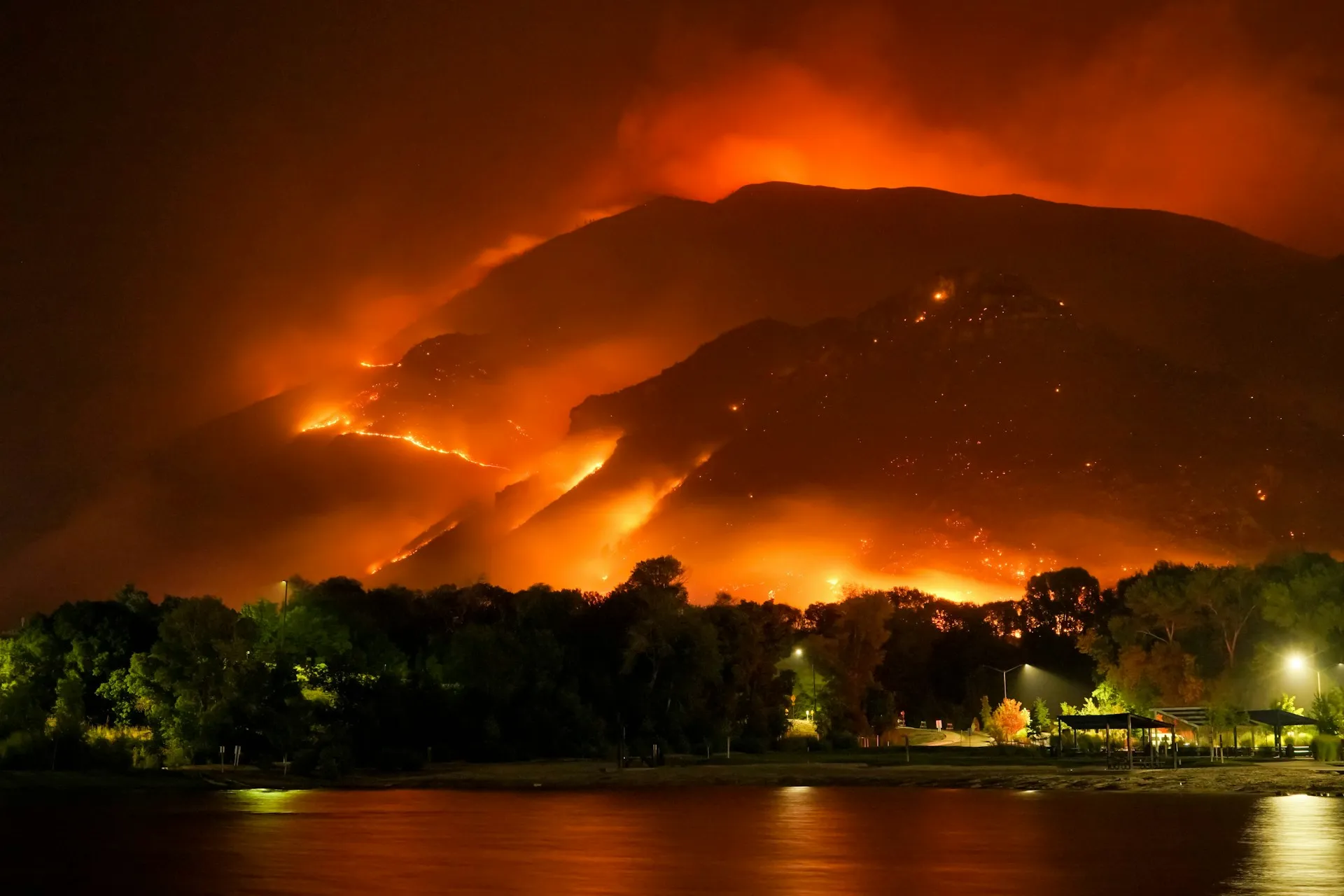 A night view of a raging wildfire consuming a mountain ridge.